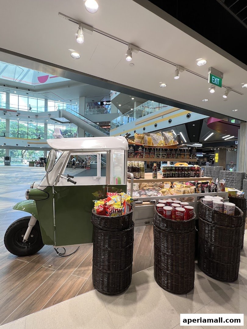 A Thai supermarket display featuring a tuk-tuk and baskets of snacks and products.