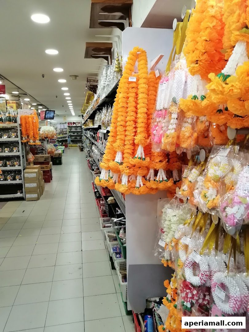 Aisle in a Thai supermarket displaying colorful flower garlands and other products on shelves.
