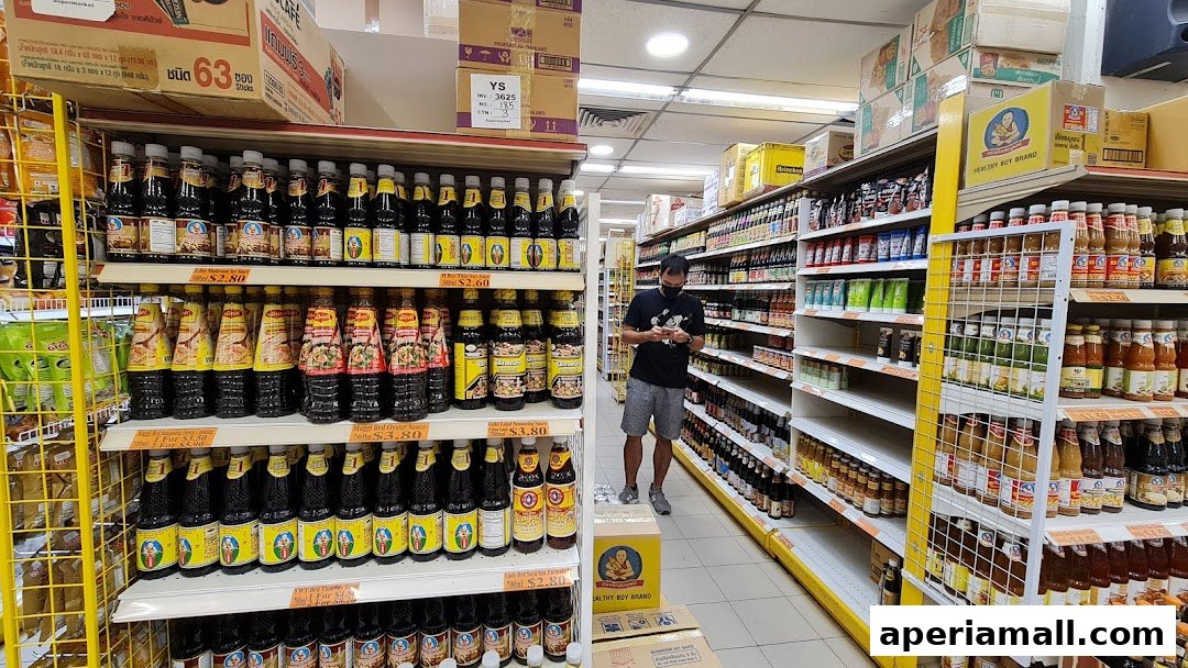A man shops in a well-stocked aisle of a Thai supermarket, with shelves full of sauces and condiments.