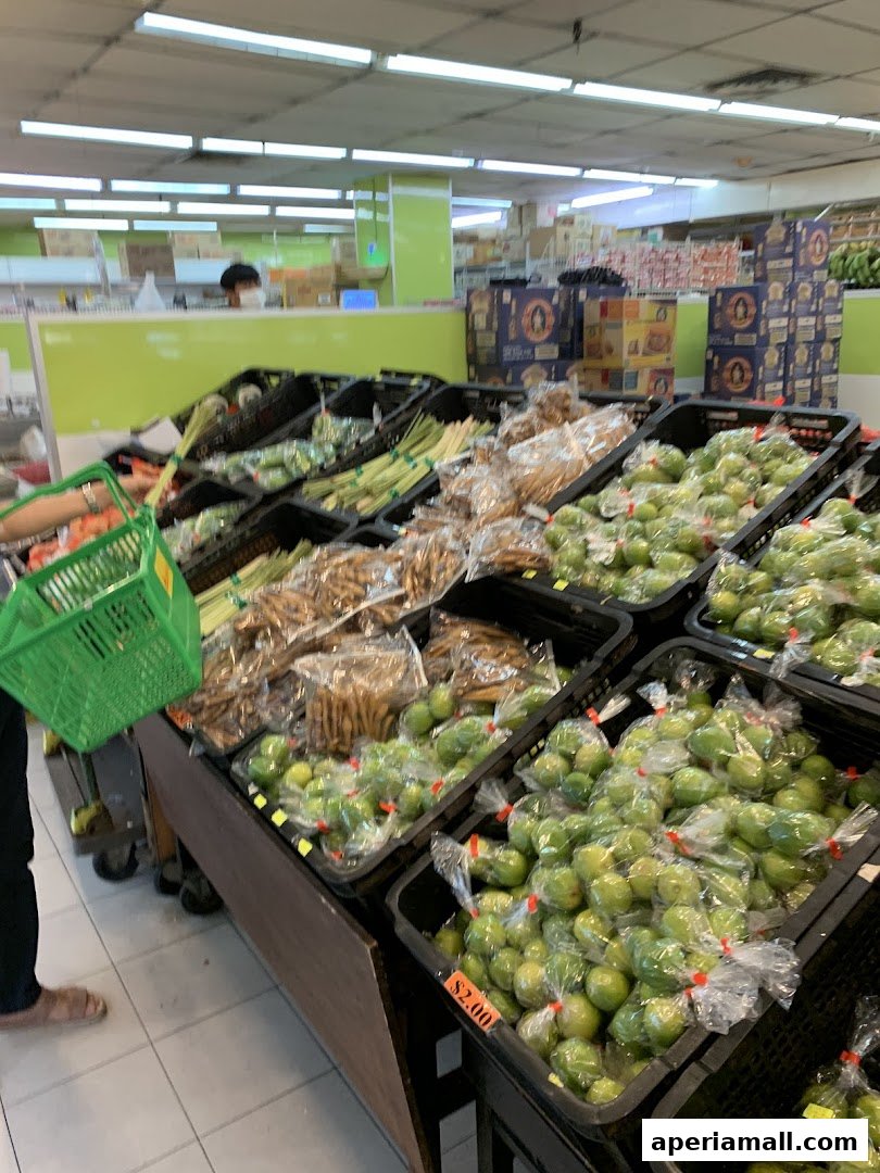 A person holds a green basket in a supermarket aisle filled with fresh produce.