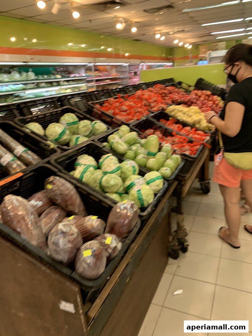 A customer browses fresh produce, including tomatoes, onions, and cabbages, at a supermarket.