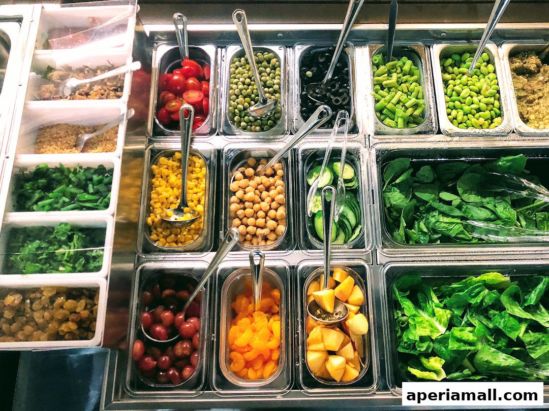 A variety of fresh salad ingredients displayed in clear containers with serving spoons.