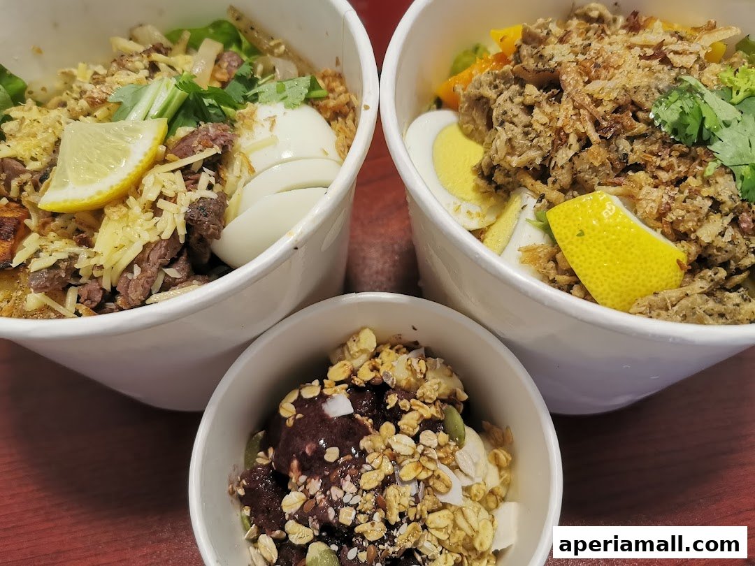 Three bowls of healthy food, two salads and one acai bowl, are displayed on a wooden surface.