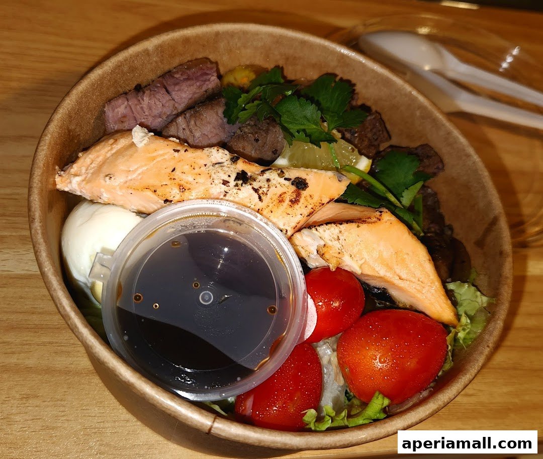 A delicious protein-packed salad bowl with salmon, steak, tomatoes, and a side of dressing.