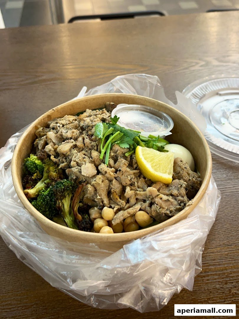 A healthy salad bowl with chicken, broccoli, chickpeas, and lemon, served in a to-go container.