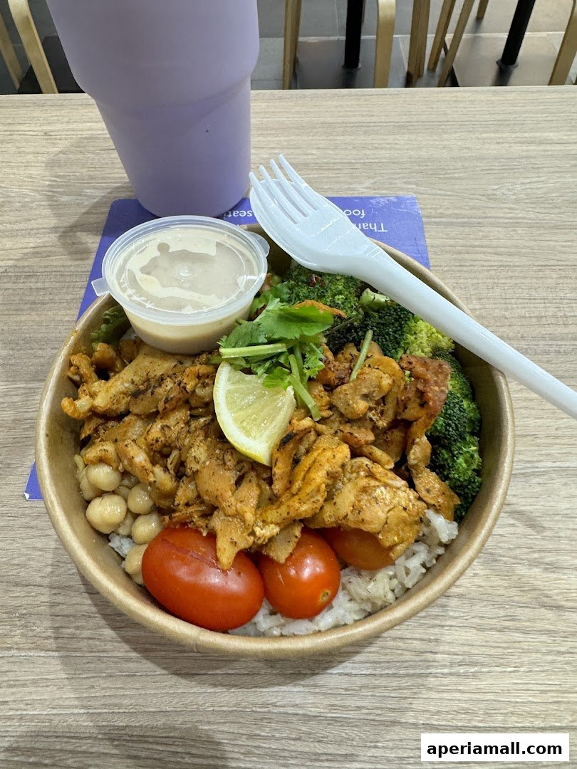 A healthy protein salad bowl with chicken, rice, broccoli, chickpeas, tomatoes, and a lemon wedge.
