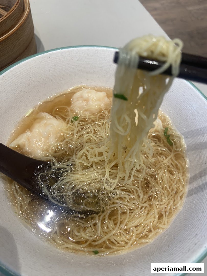 A close-up shot of a steaming bowl of wonton noodle soup with chopsticks lifting the noodles.