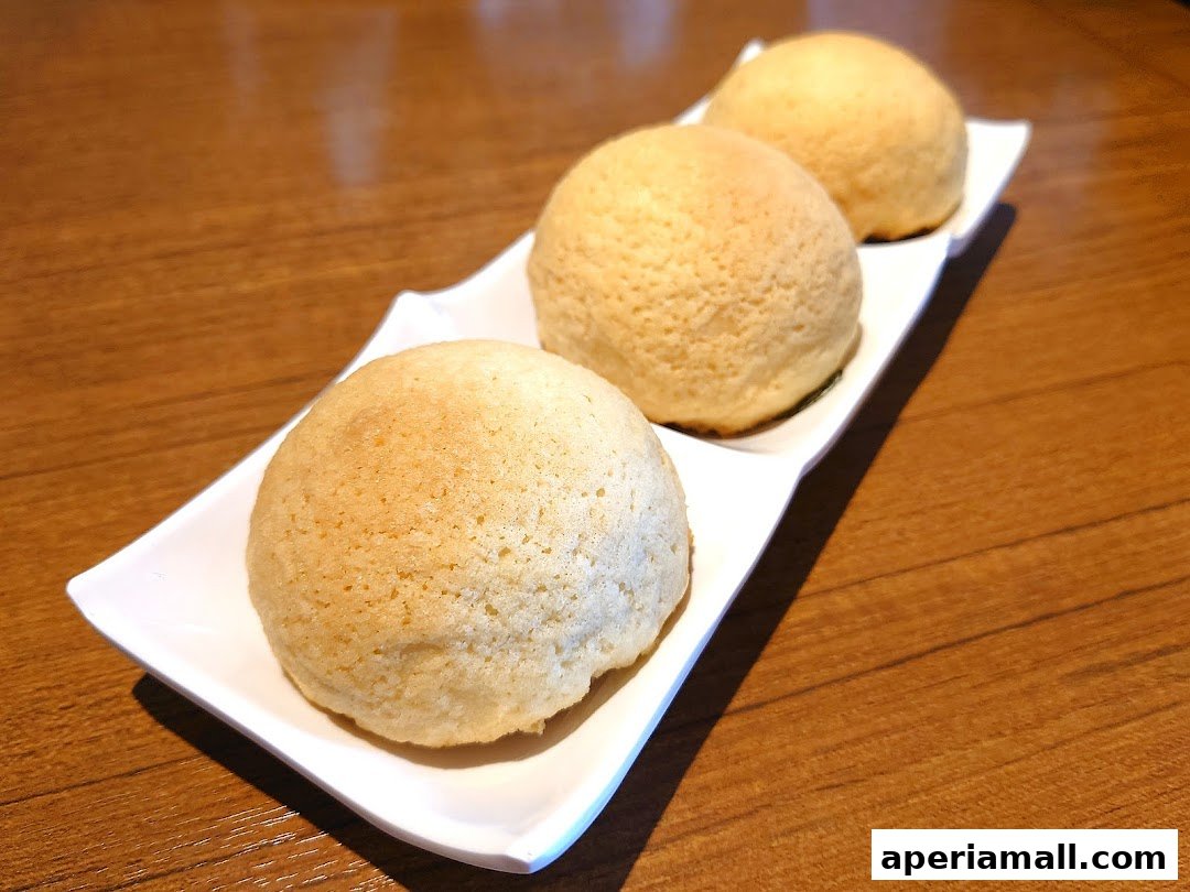 Three golden-brown baked buns served on a white rectangular plate on a wooden table.