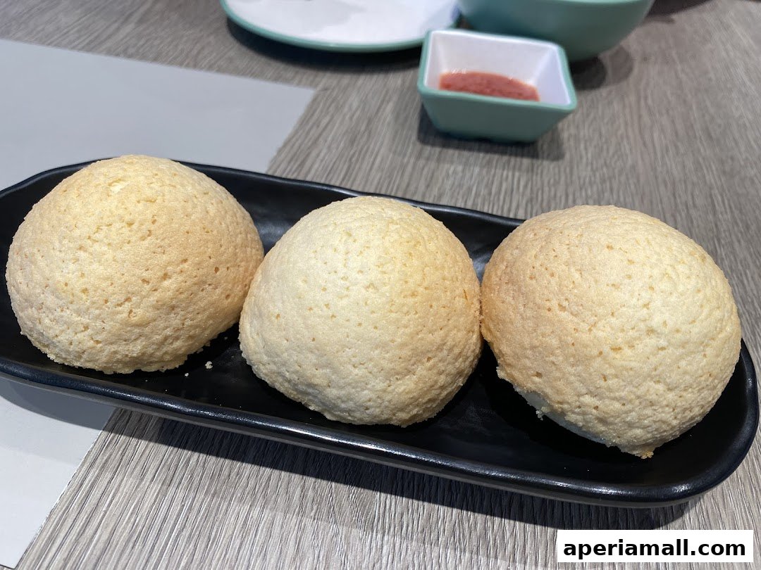 Three golden-brown baked buns served on a black plate with a small dish of sauce.