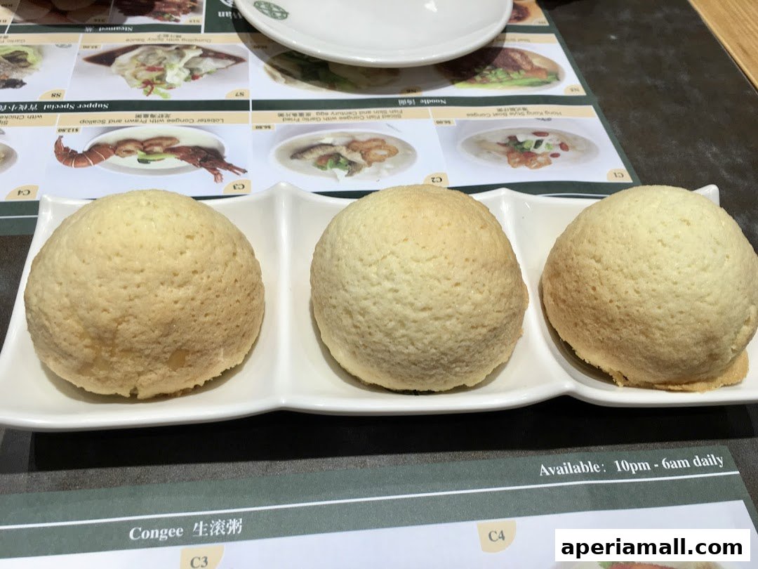 Three golden baked buns served on a white plate with menu items in the background.