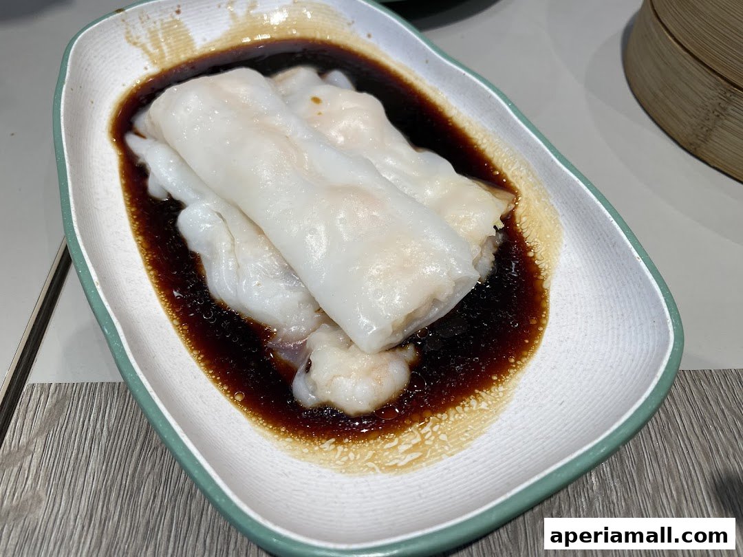 A close-up of steamed rice noodle rolls with shrimp, served in a savory sauce.