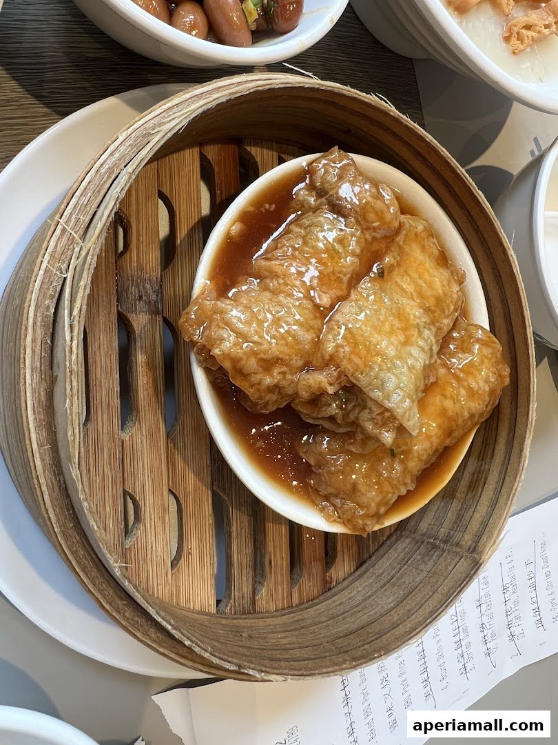 A close-up of delicious dim sum, featuring bean curd skin rolls in a savory sauce, served in a bamboo steamer.