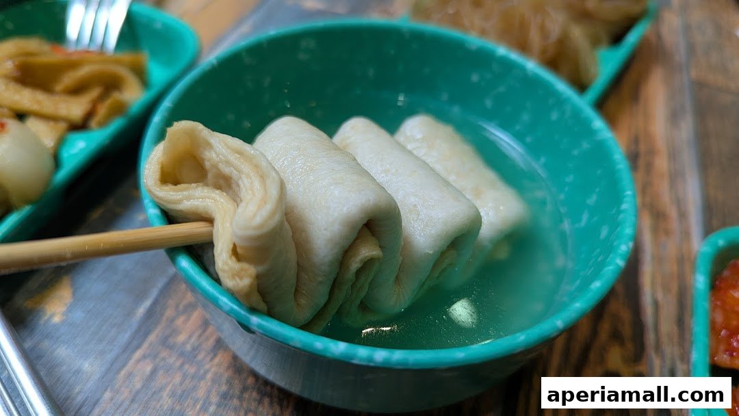 Close-up of fish cakes on a skewer in a green bowl with broth.