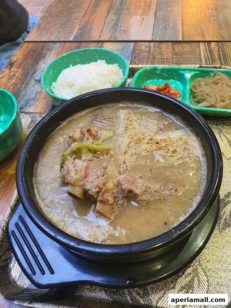 A steaming bowl of Korean gamjatang with rice and side dishes on a wooden table.