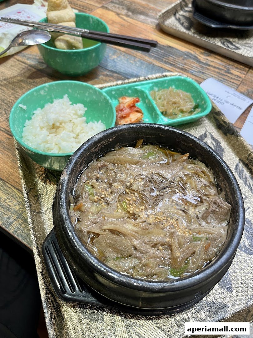 A close-up of a Korean hot pot dish with rice, kimchi, and glass noodles.