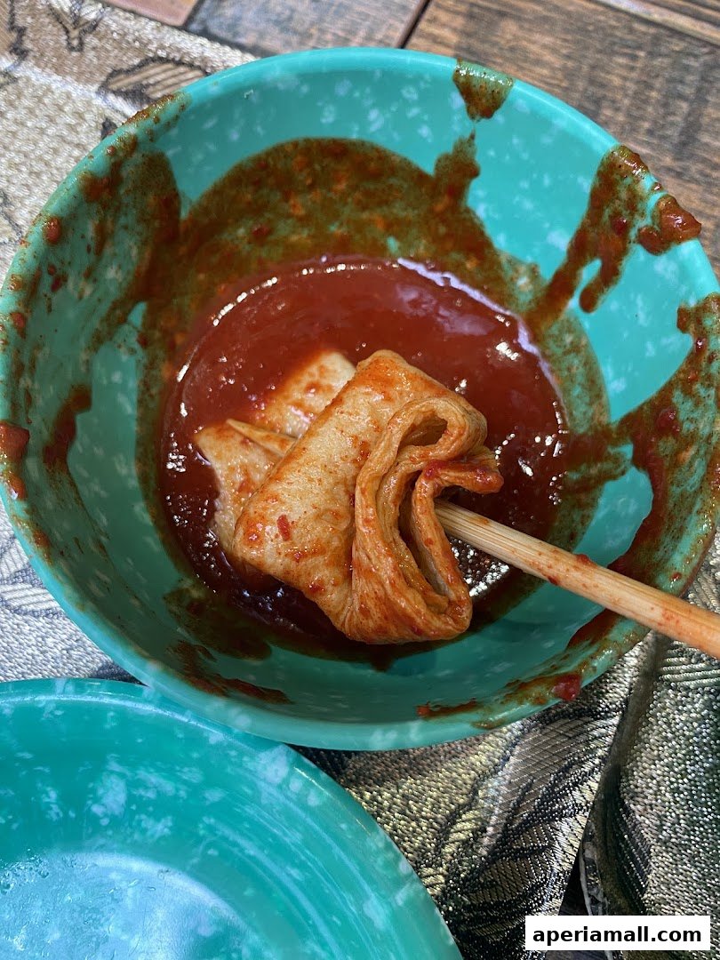A close-up of fish cakes on a skewer in a spicy red sauce.