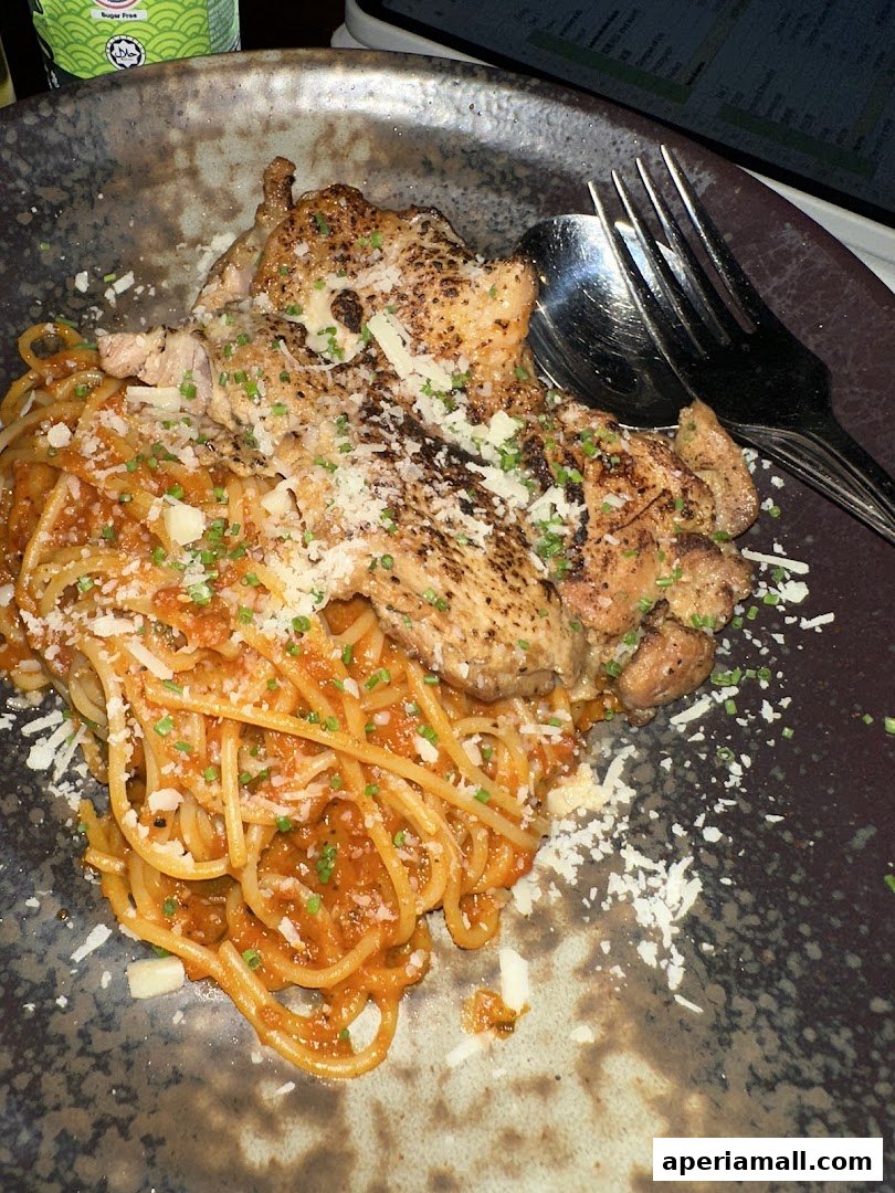 A plate of spaghetti with grilled chicken and grated cheese, served with cutlery.