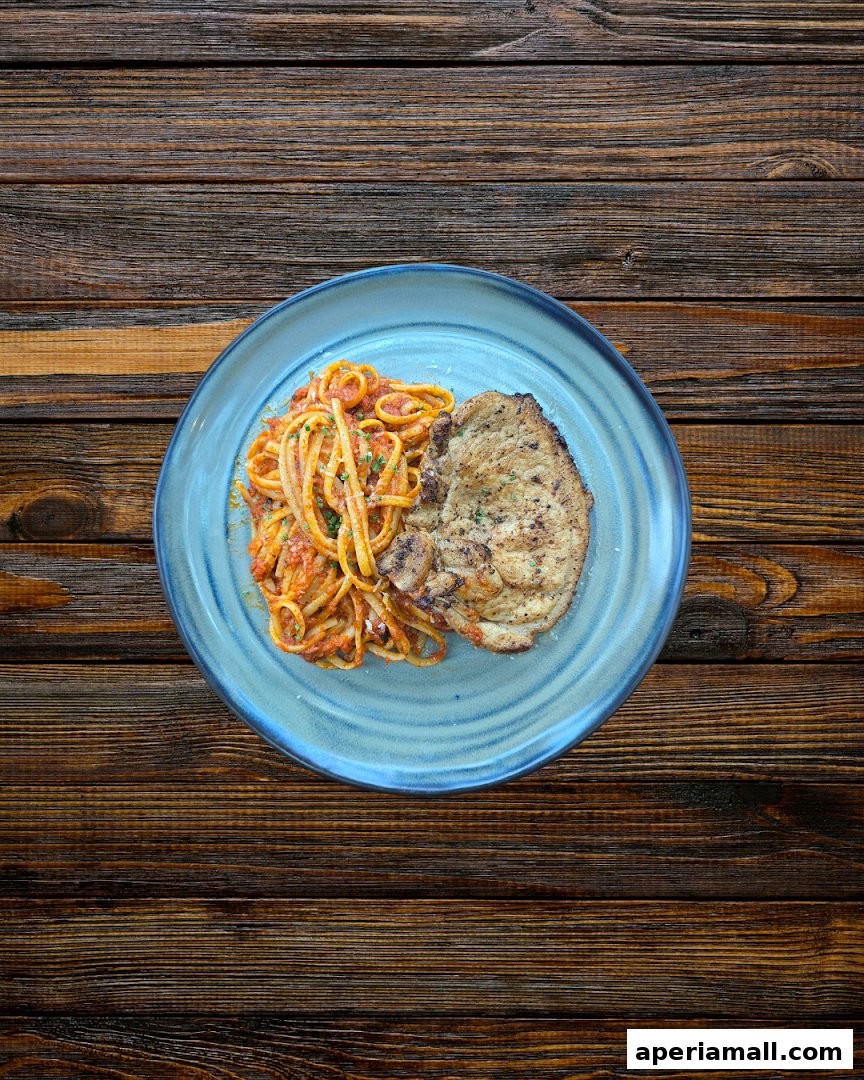 A plate of spaghetti with tomato sauce and a grilled pork chop on a wooden table.