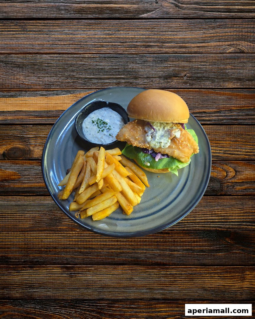 A delicious fish burger with fries and dipping sauce on a rustic wooden table.