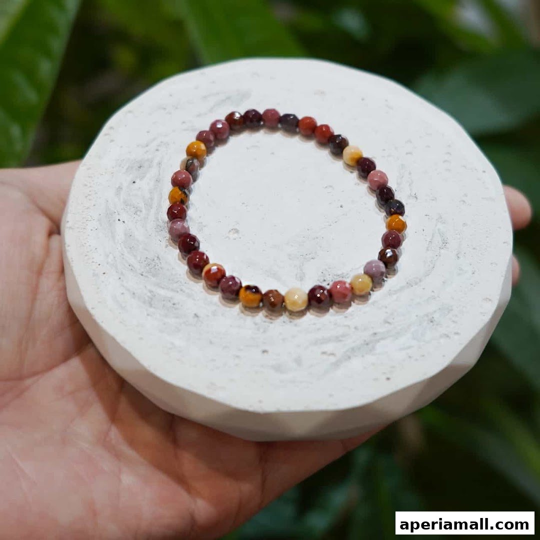 A hand holds a bracelet made of colorful faceted beads on a white display.