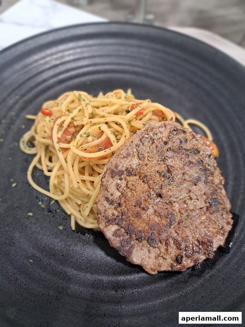 A plate of spaghetti with tomatoes and herbs, served with a grilled steak.