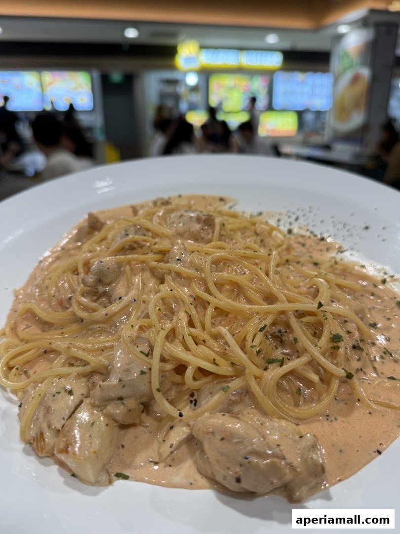 A close-up of creamy pasta with chicken pieces and herbs on a white plate.