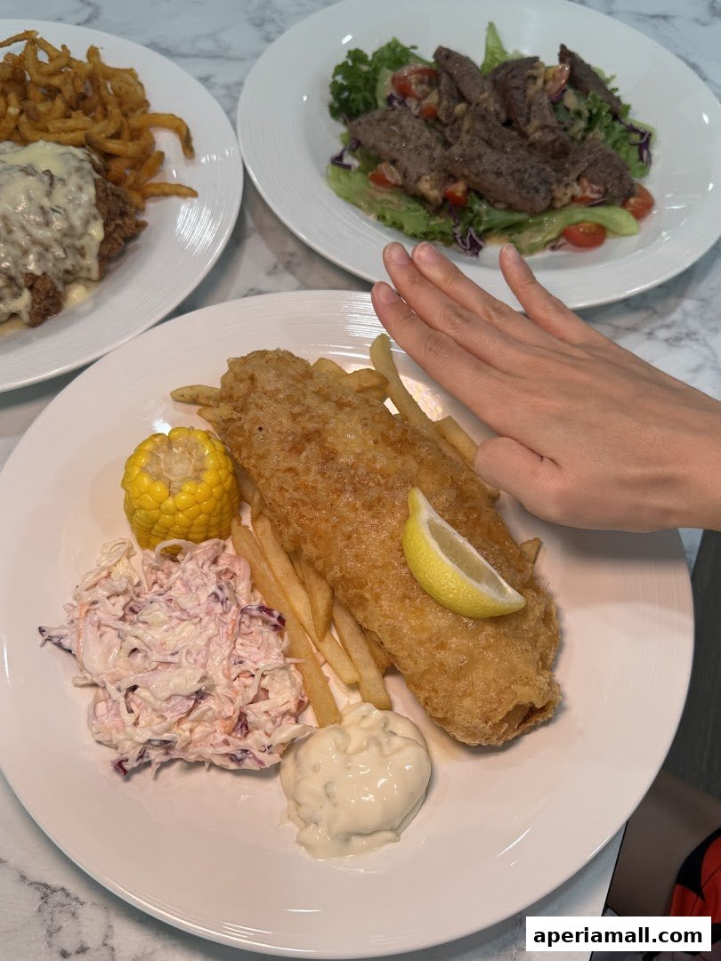 A plate of fish and chips with coleslaw and corn, next to a steak salad.