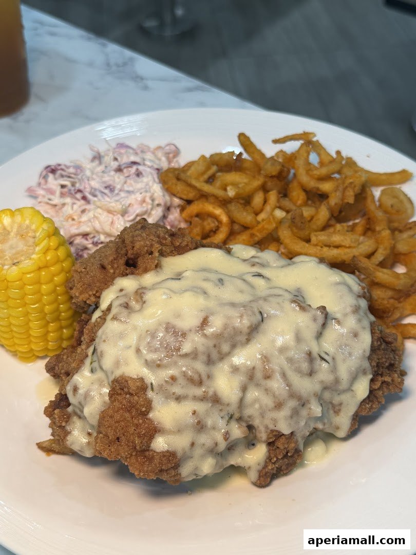A plate of fried chicken with gravy, coleslaw, curly fries, and corn on the cob.