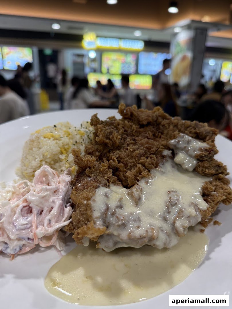 A plate of fried chicken with rice and coleslaw, drizzled with sauce.