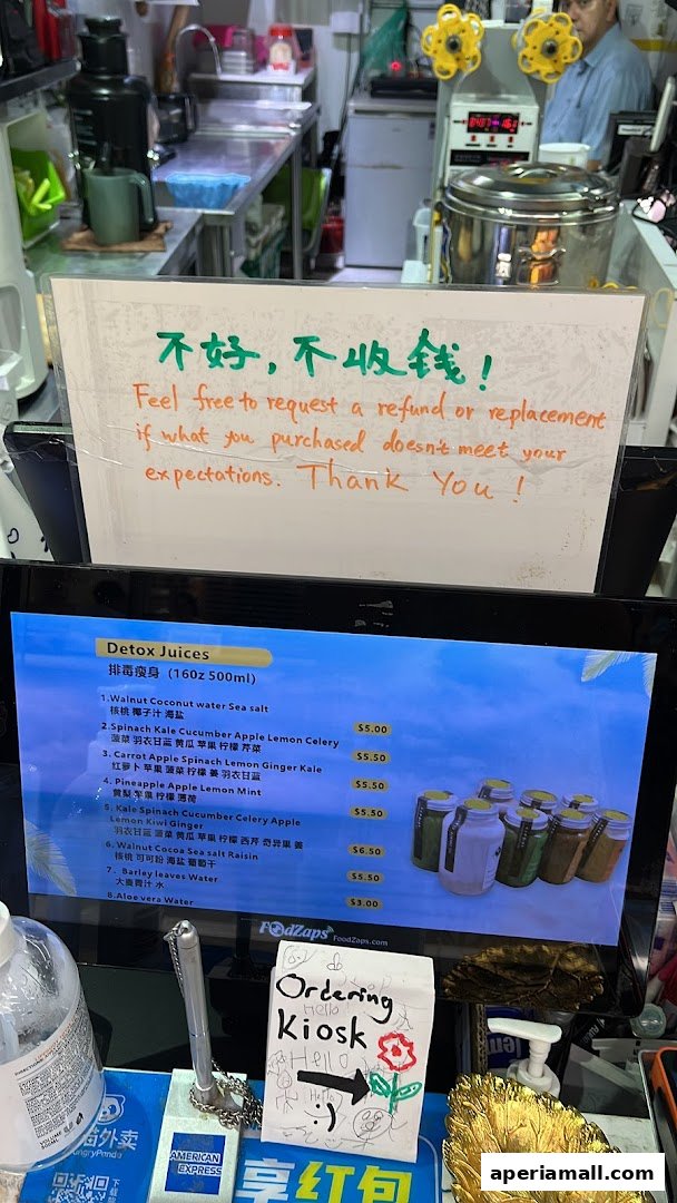A digital menu displays various detox juices with prices, alongside a refund policy sign.