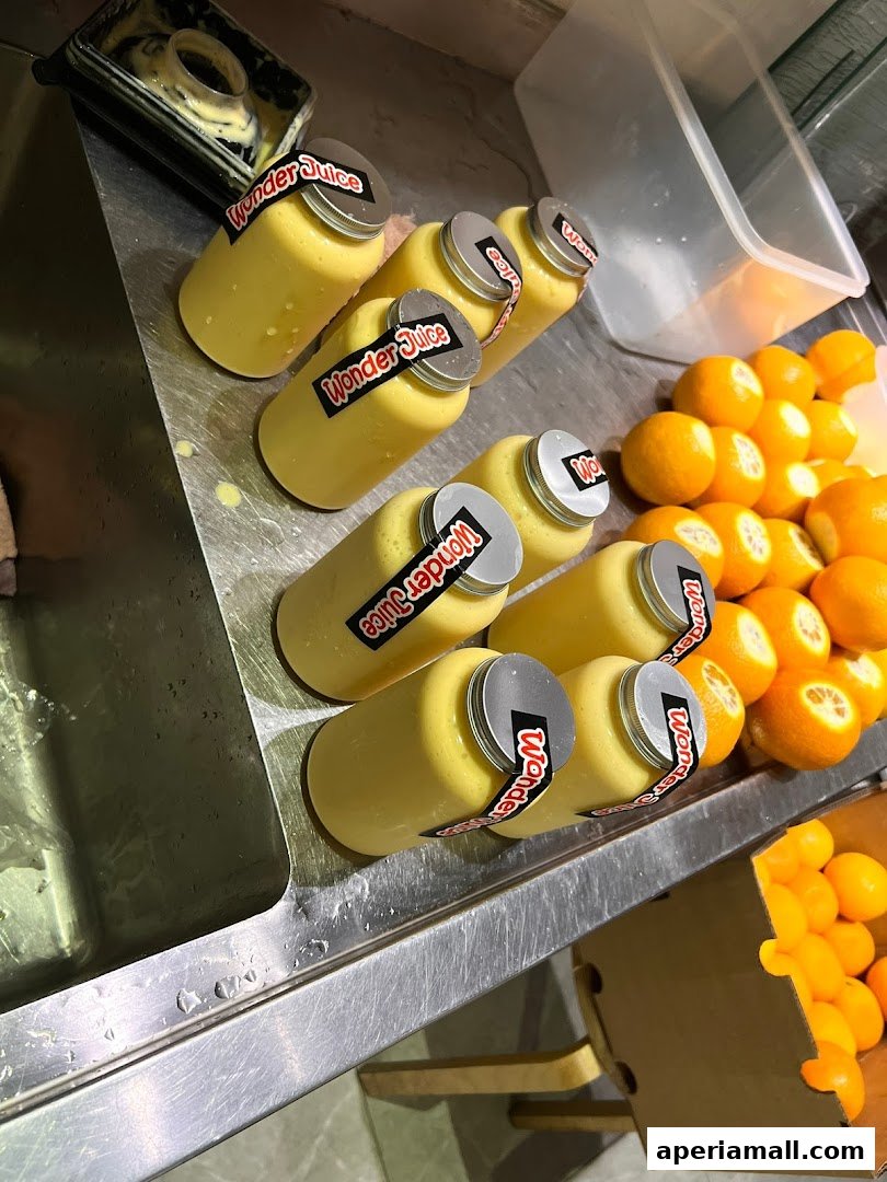 Bottles of yellow juice labeled 'Wonder Juice' next to fresh oranges.