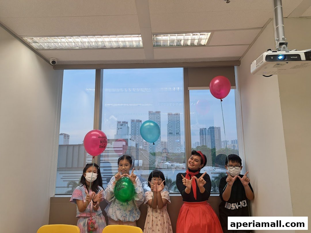 A group of children and an adult pose with balloons in front of a window with a city view.
