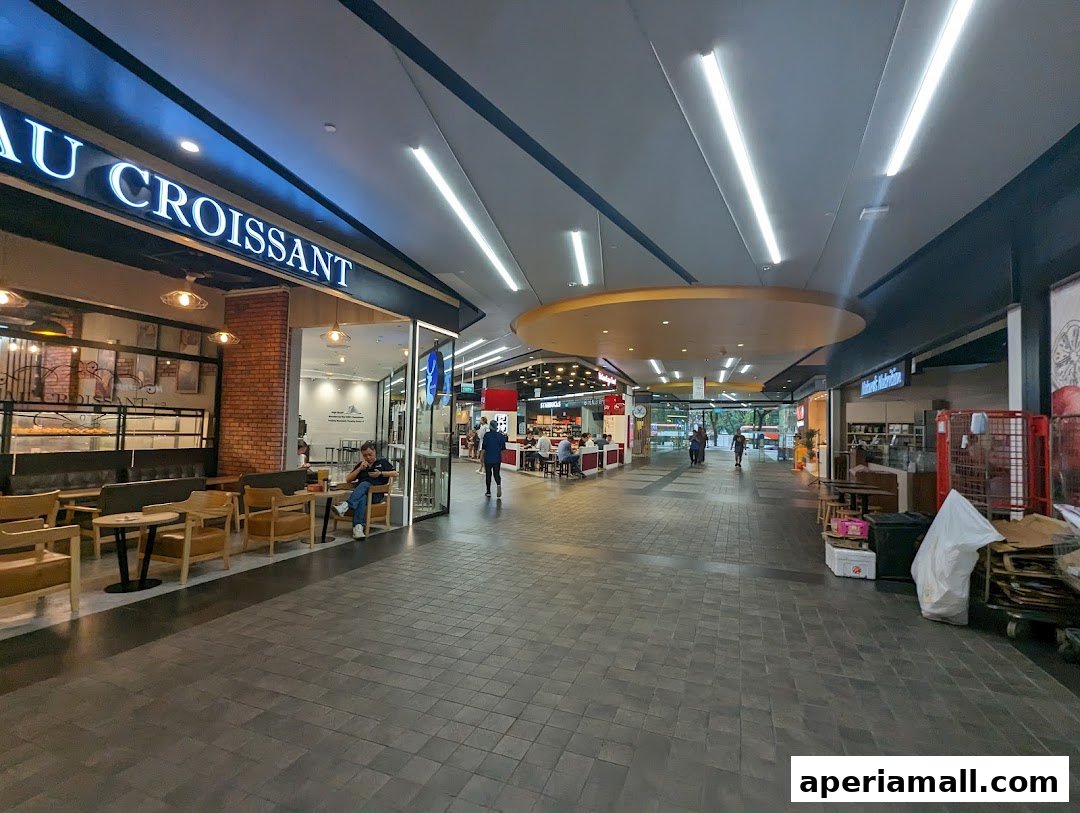 A view of a shopping mall walkway with several shops, including a cafe with outdoor seating.