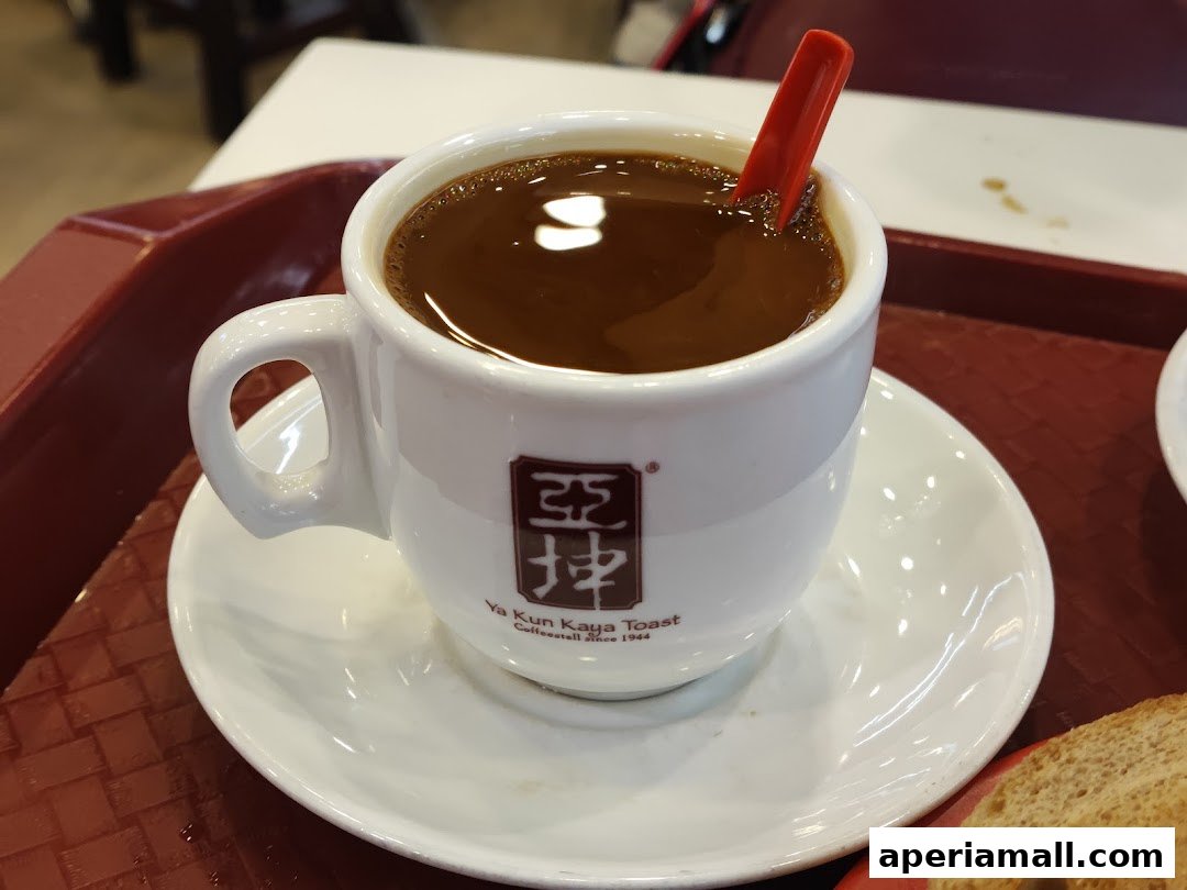 A close-up of a steaming cup of coffee with a red stirrer at Ya Kun Kaya Toast.