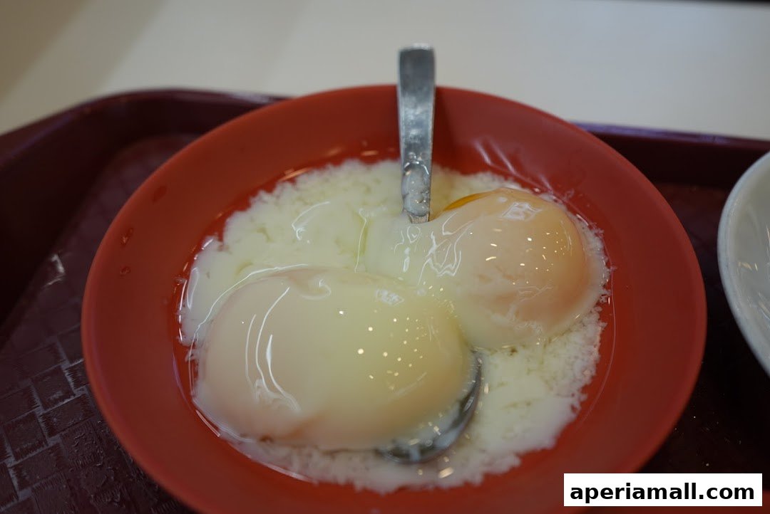 A close-up shot of two perfectly soft-boiled eggs in a red bowl with a spoon.